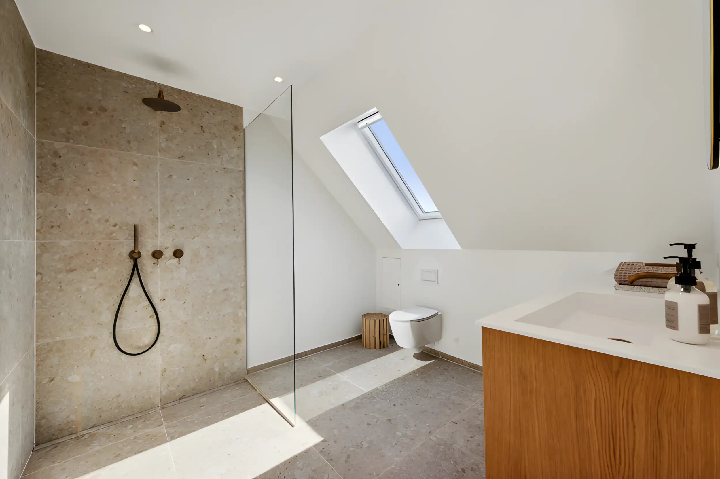 Badeværelse med bruseniche, skråvindue og minimalistisk design.