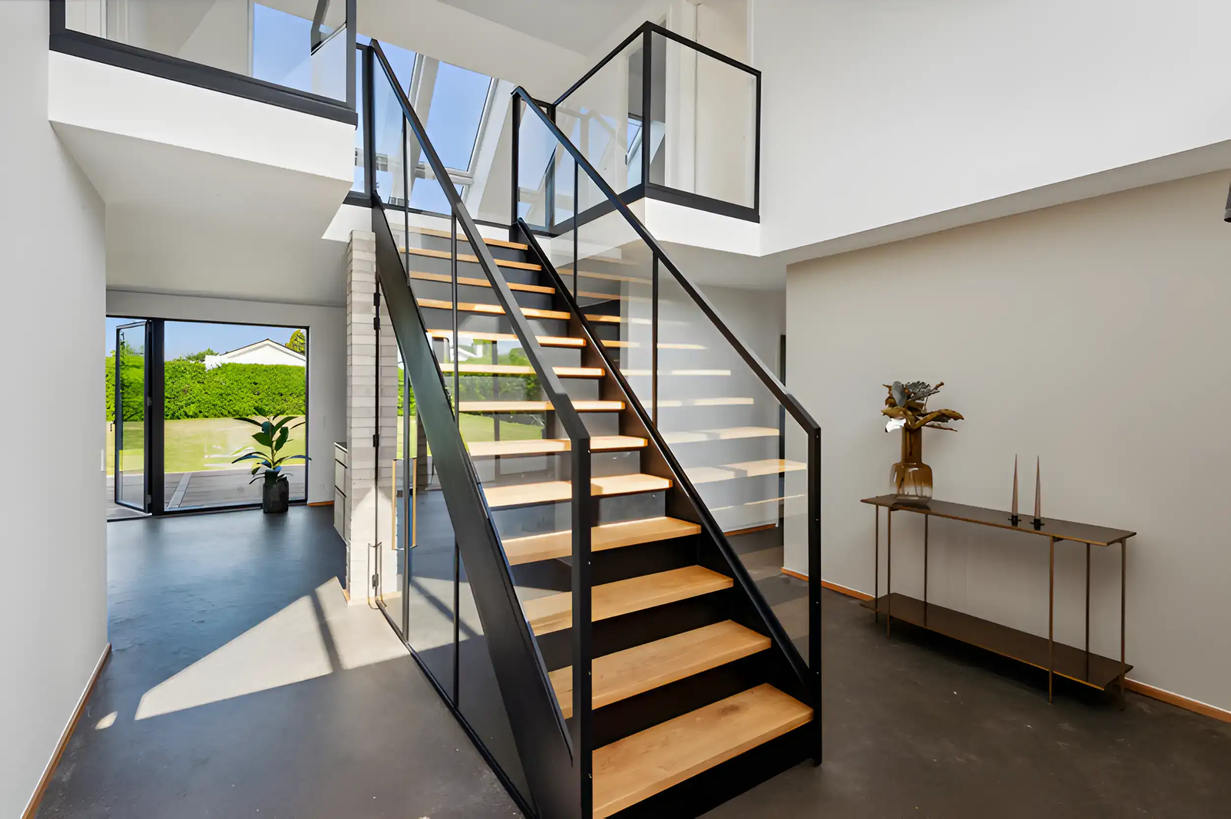 Elegant sort og træ trappe i moderne hjem med åbent design og store vinduer.
