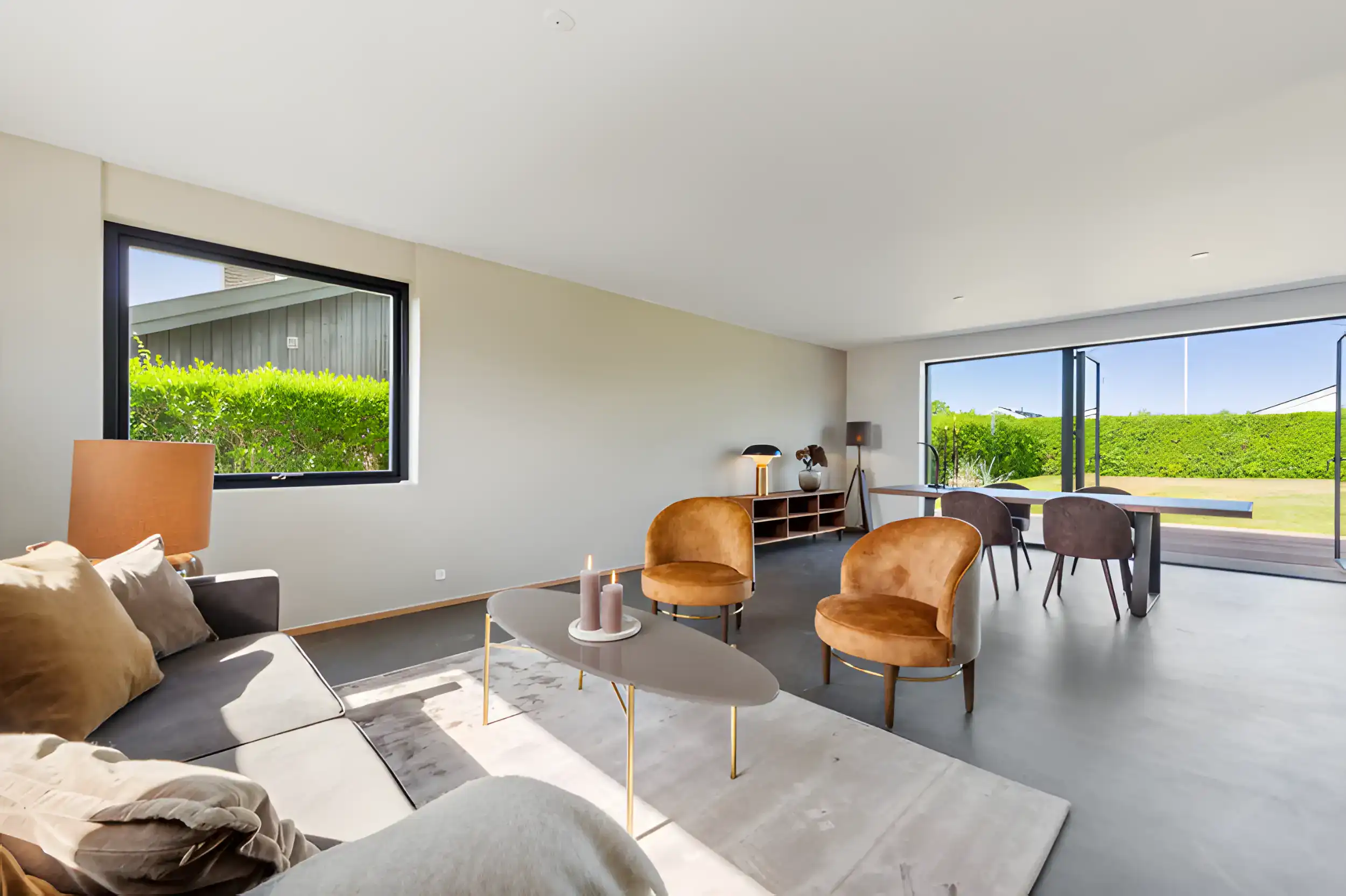 Lys stue med store vinduer, moderne møbler og grøn udsigt.