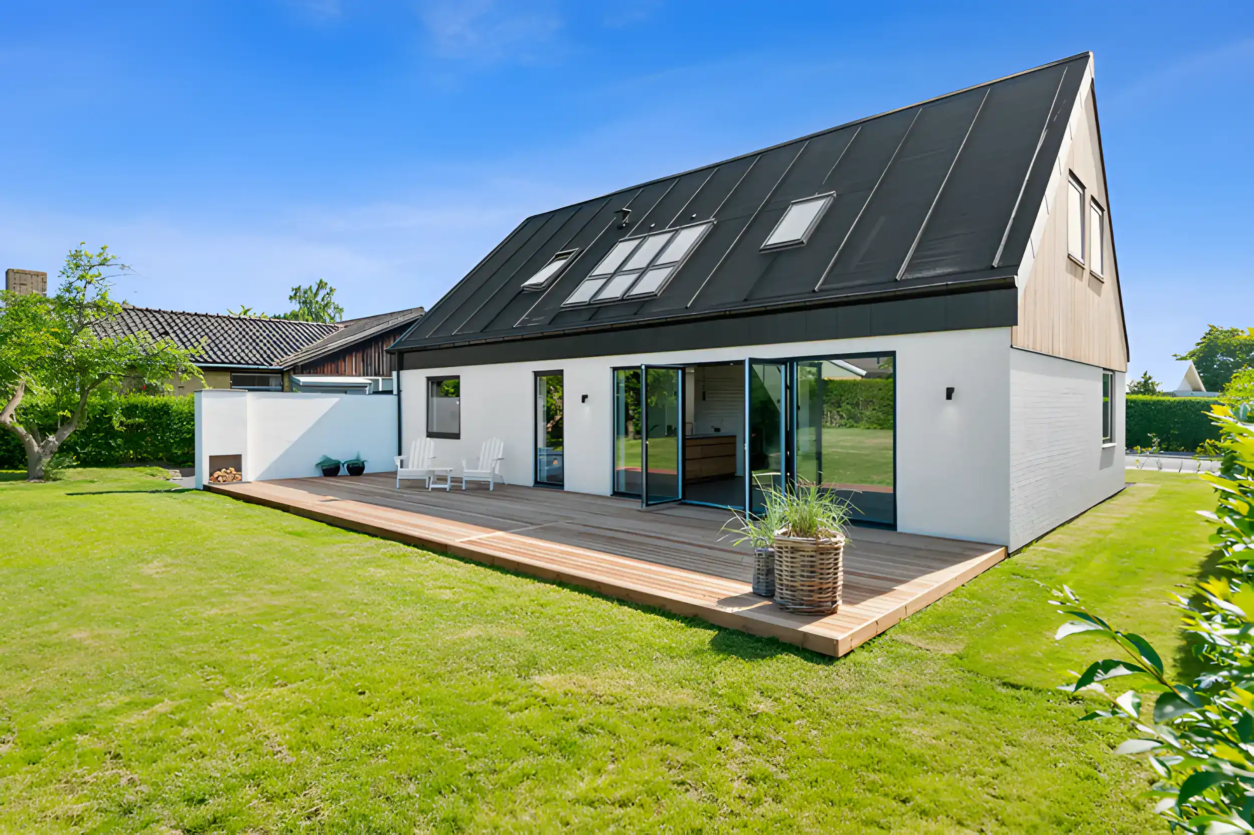 Moderne hus med stor terrasse og store vinduer, perfekt til udendørs ophold og moderne boligdesign.